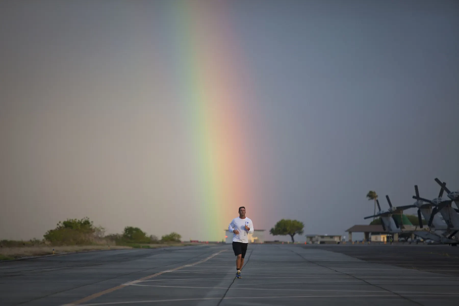 A lone runner on a long straight road under a rainbow