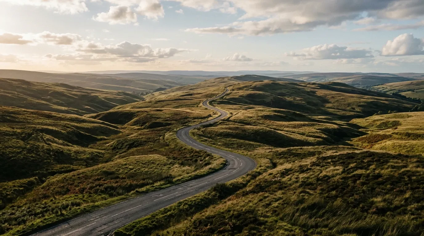 A road rising and falling over rolling hills in side light